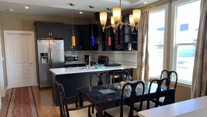 Una cocina moderna con una isla central, armarios oscuros, electrodomésticos de acero inoxidable y una lámpara de araña.
