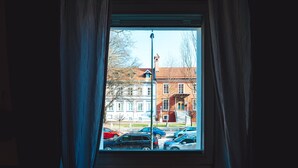 A window with a view of parked cars and a building with a red brick facade.