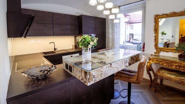 A modern kitchen with dark cabinetry, a marble island, and a glass bowl.
