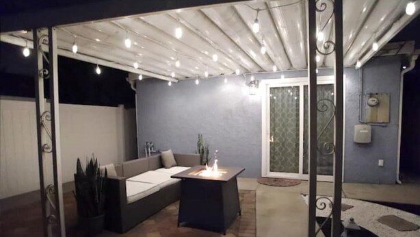 A modern outdoor patio with a built-in fire feature, a seating area, and a glass door leading to a covered entrance.