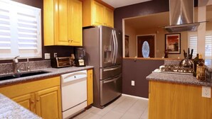 A kitchen with wooden cabinets, a stainless steel refrigerator, a dishwasher, and a granite countertop.
