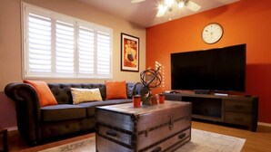 A living room with a sofa, a coffee table, a television, and a clock on the wall.