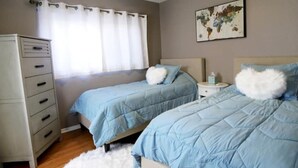 A bedroom with two beds, a dresser, a nightstand, a ceiling fan, a window with curtains, and a world map on the wall.