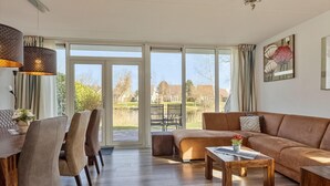 Un salón espacioso con un amplio ventanal corredera que da a un jardín, un sofá de cuero marrón, una mesa de centro de madera y un comedor con mesa y sillas.