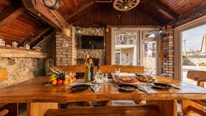 A rustic wooden dining table set with fruits, glasses, and cutlery, with a stone wall and wooden beams in the background. - Lovely home in Gracac with sauna (Gracac)