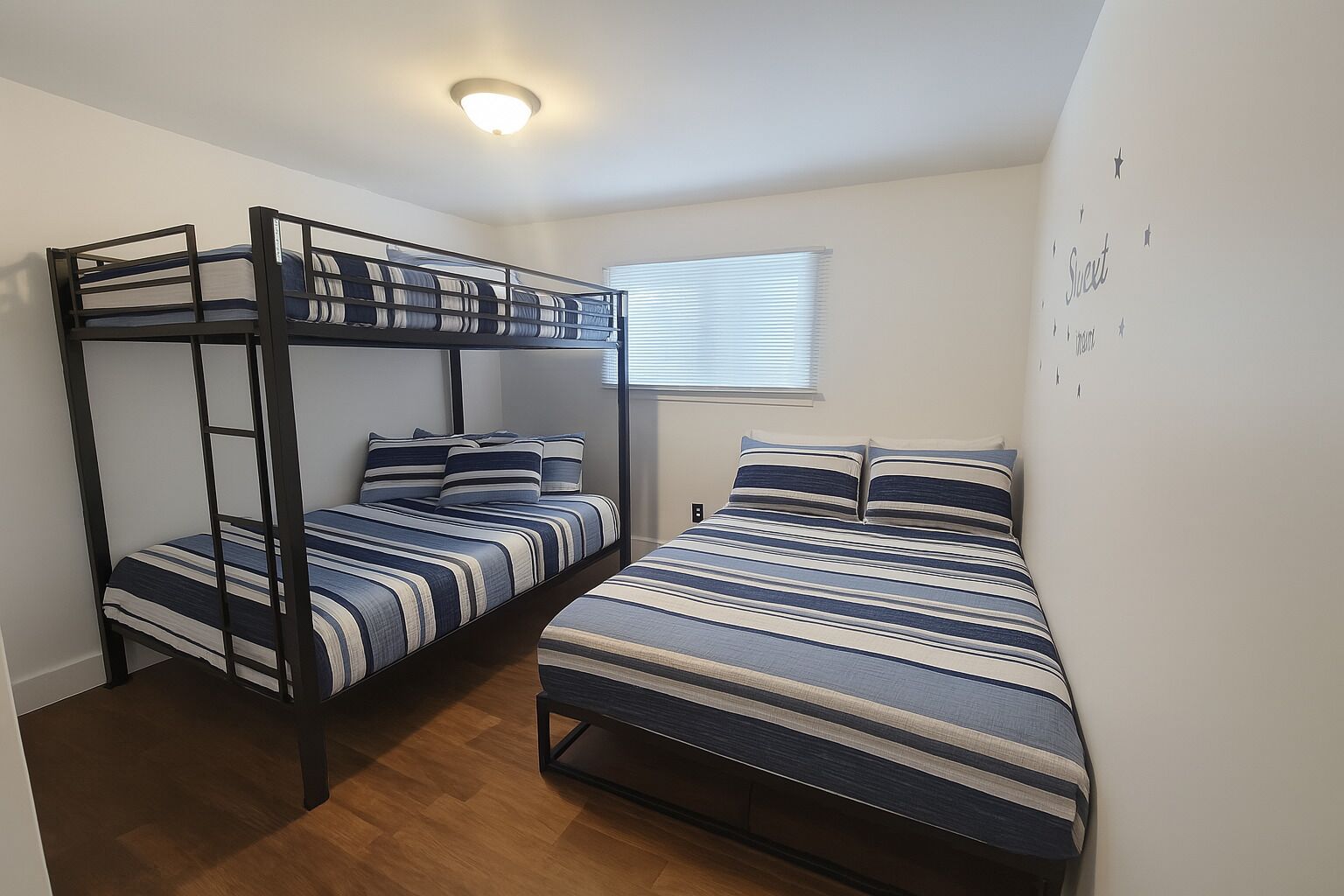 A room with two bunk beds, a window with blinds, and a wall with star decorations.