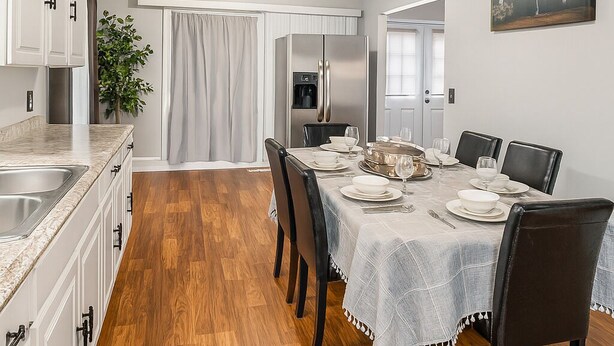 A modern kitchen with white cabinets, a stainless steel refrigerator, and a dining area with a table set for four. - "Stay in Style Downtown Grandville - Discounts for Nurses!" (Grandville)
