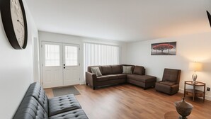 A modern living room with a sectional sofa, a chaise lounge, a small side table, and a lamp. - "Stay in Style Downtown Grandville - Discounts for Nurses!" (Grandville)