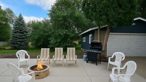 An outdoor patio with a fire pit, four white plastic chairs, and a barbecue grill. - "Stay in Style Downtown Grandville - Discounts for Nurses!" (Grandville)