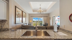 A kitchen with granite countertops, a stainless steel sink, a chandelier, and a view of a patio with a dining area.
