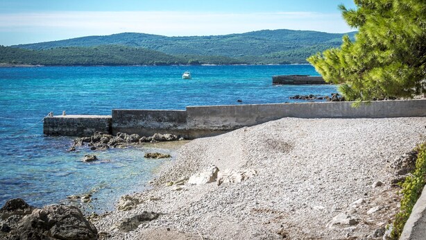 A coastal scene with clear blue waters, a rocky beach, and a distant green hill. - Stunning 3-bed House in Orebic (Orebic)
