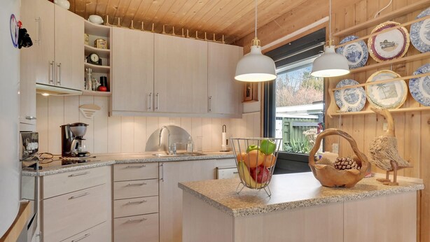 Une cuisine moderne avec des meubles de couleur bois clair, un plan de travail en granit, une machine à café et un panier de fruits.