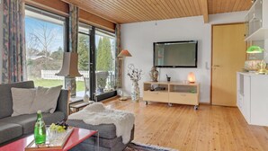 Un salon comprenant un canapé, une table basse avec une bouteille et des verres, un téléviseur, un meuble et une porte.