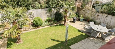 A backyard with a lawn, a patio table with chairs, and various plants.