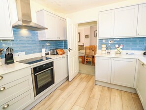 A modern kitchen with white cabinets, a blue tiled backsplash, a built-in oven, and a dining area with a wooden table and chairs. - Altair (Freshwater)