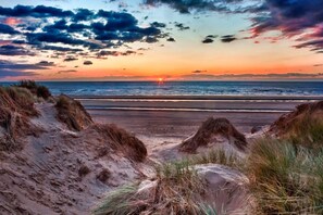 Una playa con dunas y el océano al atardecer.
