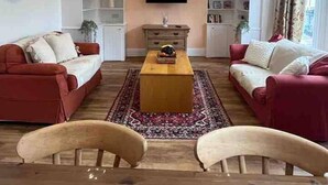 A living room with two red sofas, a wooden coffee table, and a flat-screen TV mounted on the wall. - Stunning 4-bed Apartment in Cambridge (Cambridge)