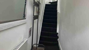 A narrow hallway with a black staircase, a metal rack, and a window with a decorative frame. - Stunning 4-bed Apartment in Cambridge (Cambridge)
