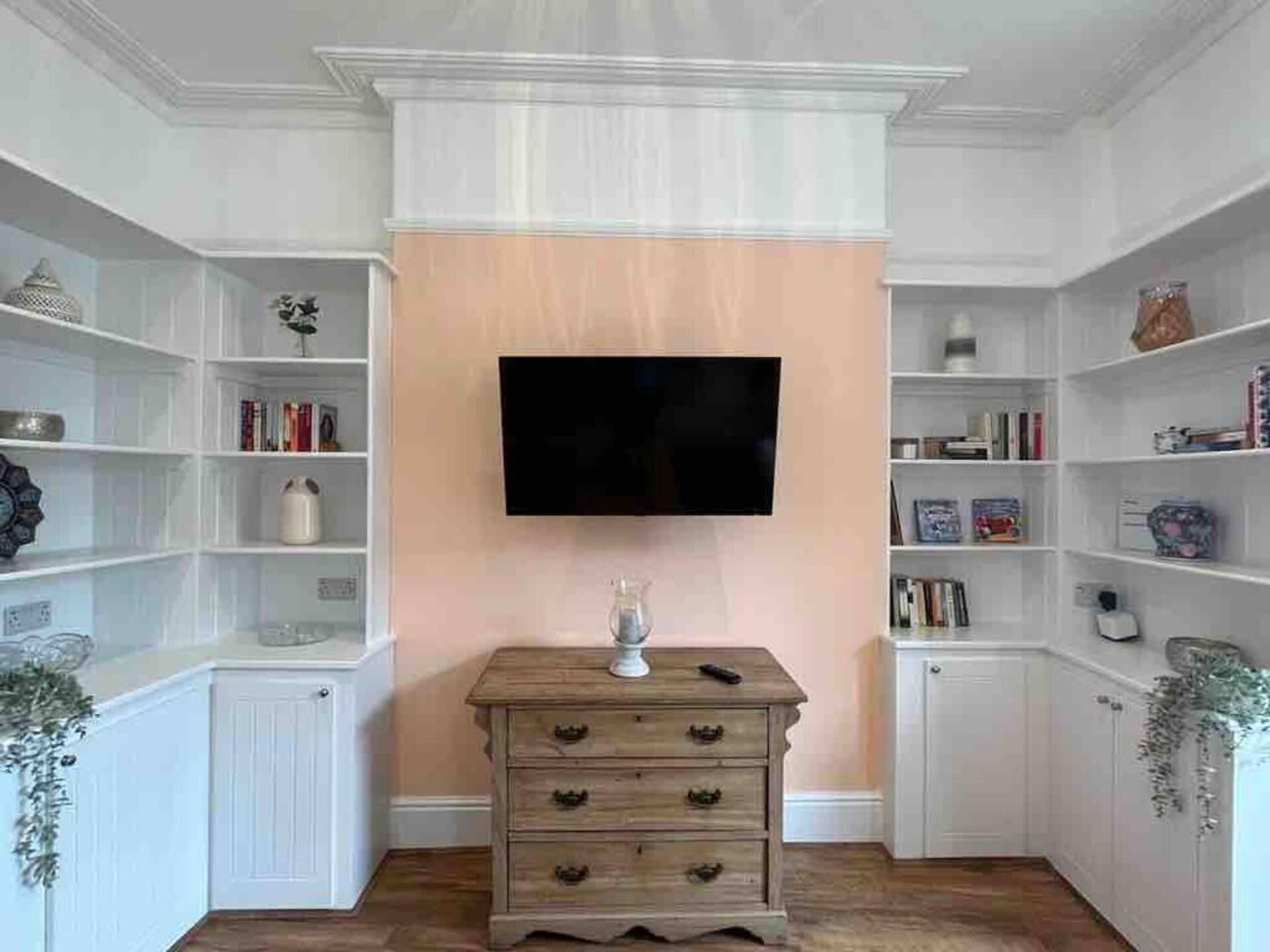 A room with a flat-screen TV mounted on a wall, surrounded by white shelving units filled with books and decorative items.
