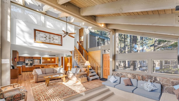 A spacious living room with a staircase, wooden floors, and large windows offering a view of the outdoors.