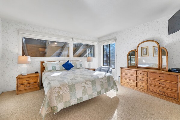 A bedroom with a large bed, wooden nightstands, a dresser, and a mirror.