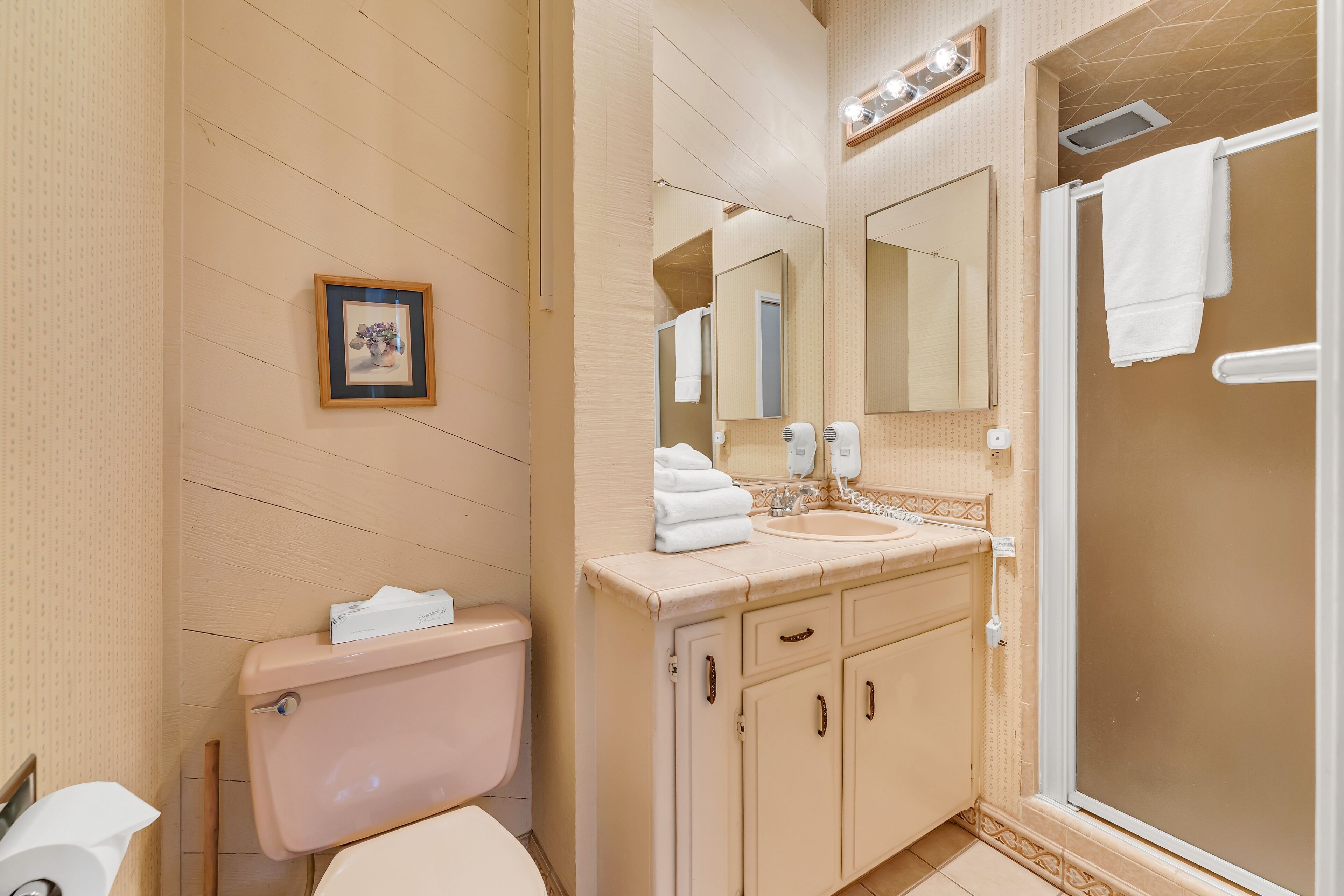 A bathroom with a toilet, sink, mirror, and shower.