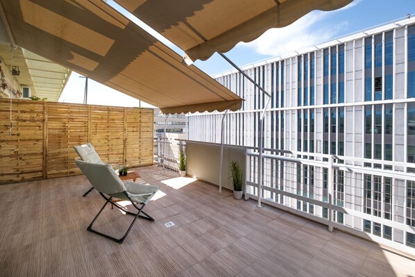 A modern outdoor balcony with a wooden floor, a white chair, and potted plants.