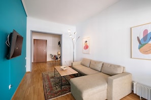A modern living room with a sectional sofa, a coffee table, a TV mounted on a teal wall, and a dining area in the background.