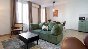 Un salon avec un canapé vert, une chaise en bois, une petite table et un tapis à motifs.