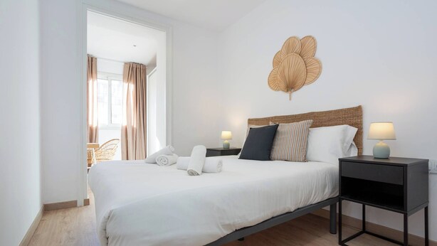 Une chambre moderne avec un grand lit, deux tables de chevet, un luminaire fixé au mur et une vue sur l’extérieur.