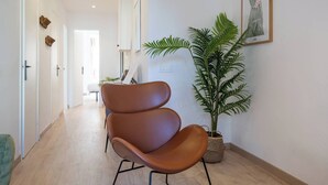 Un couloir avec un fauteuil en cuir marron, une plante en pot et une œuvre d’art encadrée accrochée au mur.