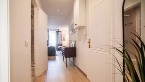 A hallway with wooden flooring, white walls, and a door on the right. There is a plant in the foreground. - 12CRC1038 - Refurbished Big & Cozy Apartment (Barcelona)