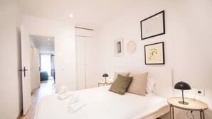 A modern hotel room with a large bed, a bedside table with a lamp, and a view of the hallway. - 12CRC1038 - Refurbished Big & Cozy Apartment (Barcelona)