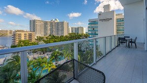 A balcony with a view of a swimming pool, palm trees, and high-rise buildings.