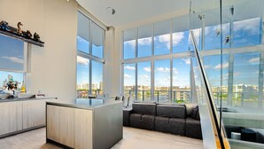 A modern kitchen with a central island, large windows offering a city view, and a glass railing overlooking the city.