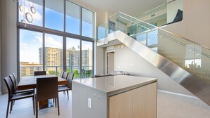 A modern kitchen with a central island, large windows, and a staircase leading to an upper level.