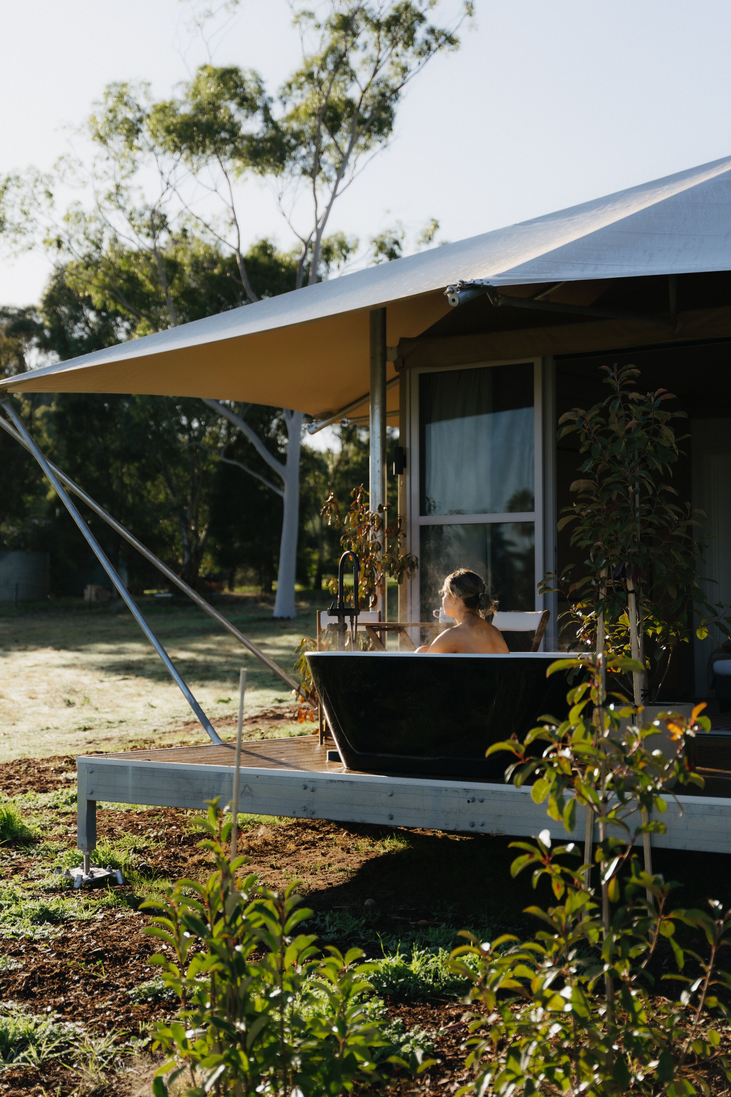 A person sitting under a tent-like structure with a window, surrounded by greenery and trees.