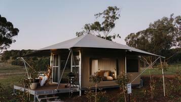 A modern, open-air tent-style accommodation with a spacious interior, a balcony, and a view of the surrounding landscape.