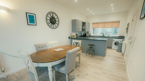 Een moderne keuken met een eethoek, met een houten tafel, witte stoelen en een inbouw wasmachine.