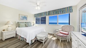 A bedroom with a large bed, a ceiling fan, a window with a view of the ocean, and wicker furniture. - Needle Rush Point D33 | Walk to FloraBama | 2 Pools | Boat Slips | My Beach Getaways (Pensacola)