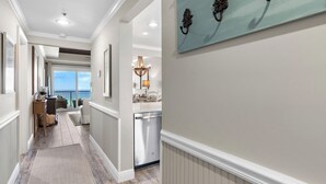 A hallway with a view to a balcony, a chandelier, and a dishwasher.