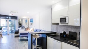 Uma cozinha moderna com micro-ondas embutido, pia e área de refeições com mesa de vidro e sofá azul.