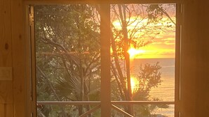 A wooden-framed sliding door with a view of a sunset over a beach with palm trees. - BRAND NEW & Waterfront 2bedroom 2bath ~ Lanai (Current)