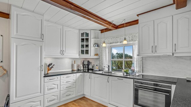 A modern kitchen with white cabinetry, a built-in oven, and a large window providing natural light. - 7 bedroom stunning home in Outrup (Outrup)