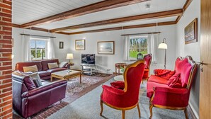 A living room with a brick wall, a wooden ceiling, a sofa, a red chair, and a television. - 7 bedroom stunning home in Outrup (Outrup)