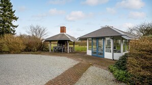 A covered outdoor seating area with a table and chairs, a small brick structure with a chimney, and a glass-enclosed room with a door. - 7 bedroom stunning home in Outrup (Outrup)