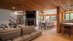 Amplia sala de estar con chimenea, comedor con mesa y sillas de madera, y cocina con barra.