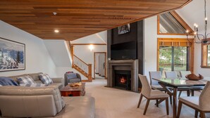 Amplia sala de estar con chimenea, zona de comedor y escalera que sube a otro nivel.