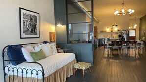 Een gezellige kamer met een bed, een klein krukje, een zithoek en een keuken op de achtergrond.
