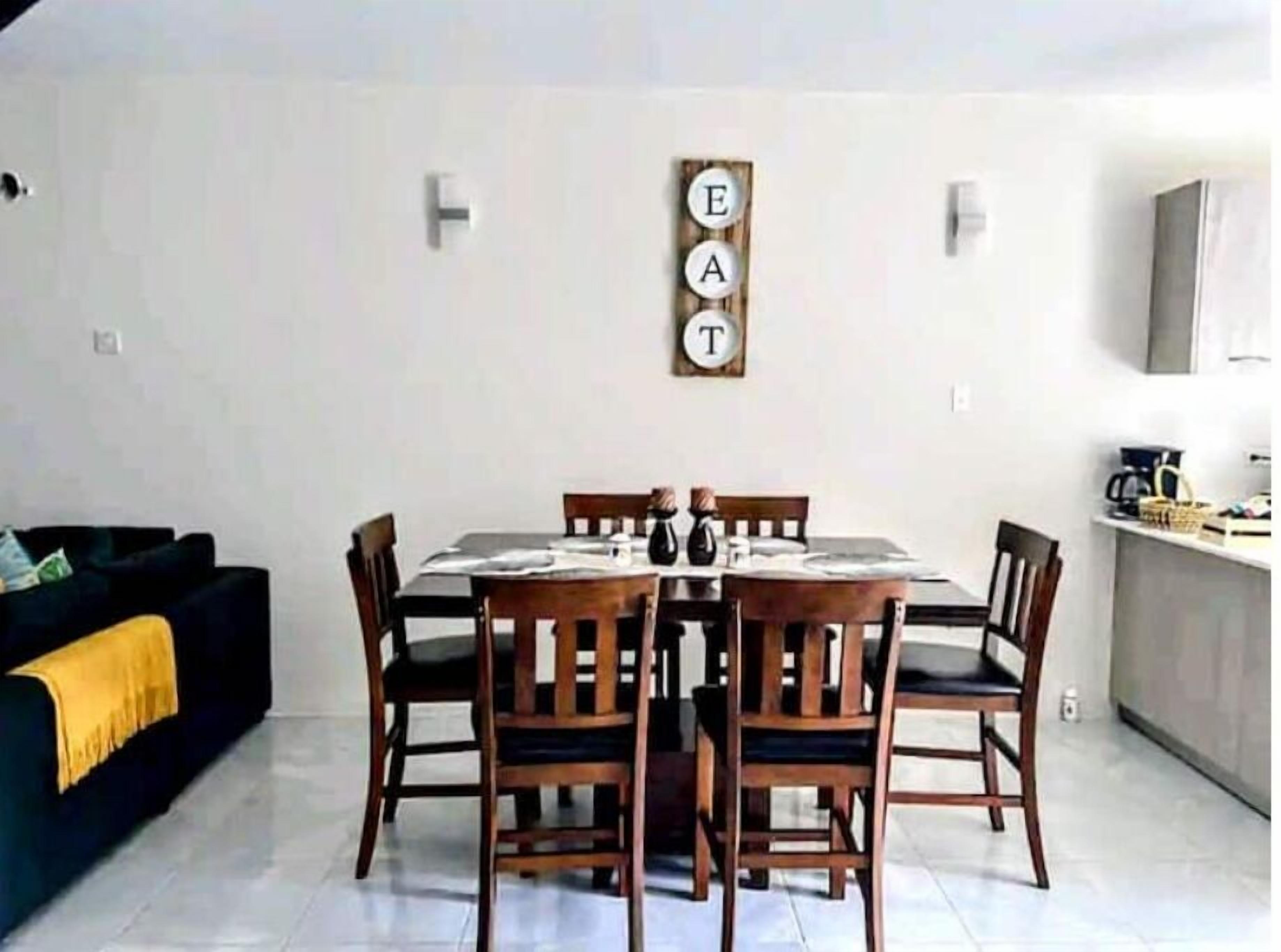 Ein Essbereich mit Tisch und Stühlen, einer schwarzen Couch und einem an der Wand befestigten Schild mit der Aufschrift 'EAT'.